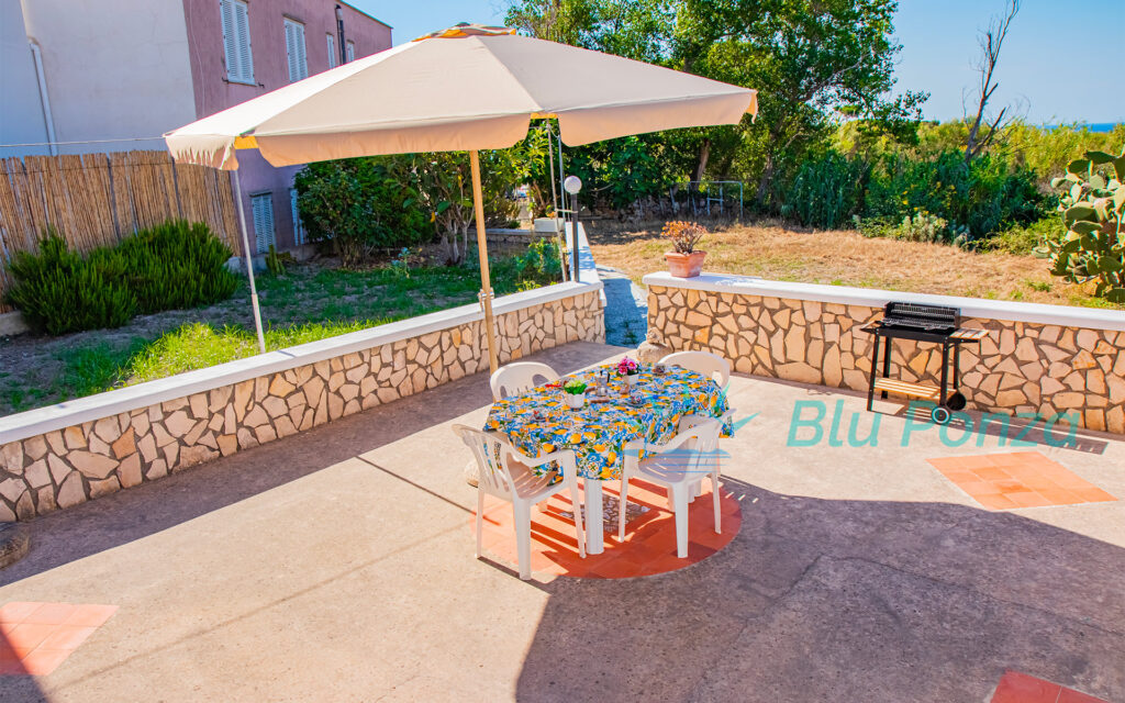Terrazza dell'Appartamento Londra a Ponza con tavolo da pranzo all'aperto, ombrellone e barbecue, situata nella zona Le Forna vicino Cala dell'Acqua - Blu Ponza.